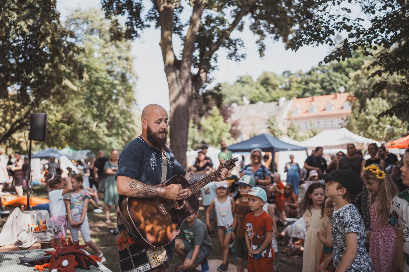 Hudebník s kytarou hraje dětem v publiku na festivalu Živé Teplice